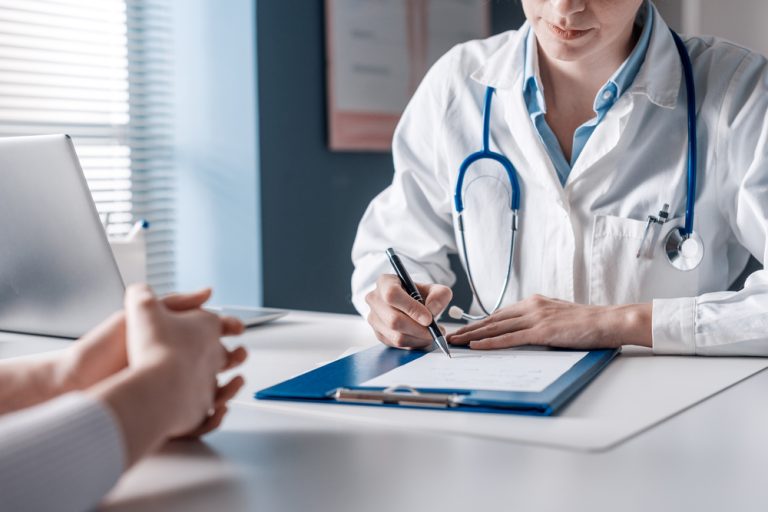 Doctor,Sitting,At,Desk,And,Writing,A,Prescription,For,Her