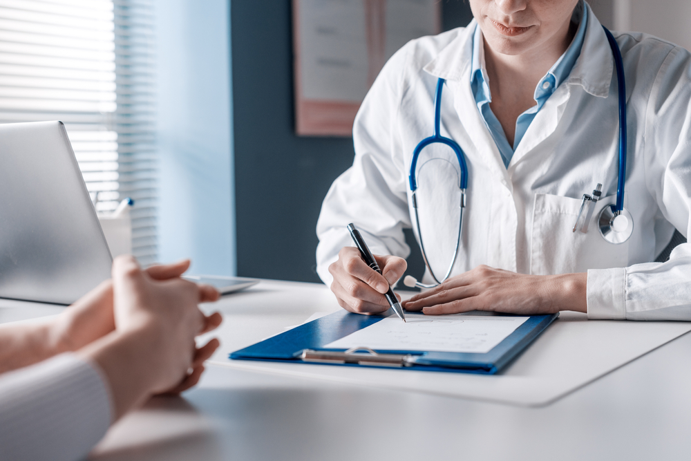 Doctor,Sitting,At,Desk,And,Writing,A,Prescription,For,Her